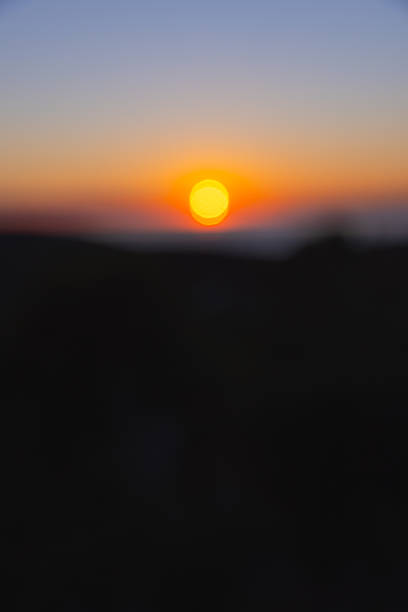 An abstract, out-of-focus image capturing the glowing sun as it sets over the Adriatic Sea, casting warm orange and purple hues across the sky. The soft blur effect gives the scene a dreamy, ethereal quality, emphasizing light, color, and mood over form. This artistic photograph evokes a sense of peace, nostalgia, and contemplation—ideal for background use, design compositions, or editorial themes focused on emotion and atmosphere.