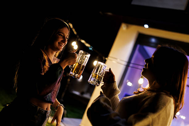 istock Two friends enjoying a festive evening outdoors while celebrating with drinks under decorative lights 2221219194