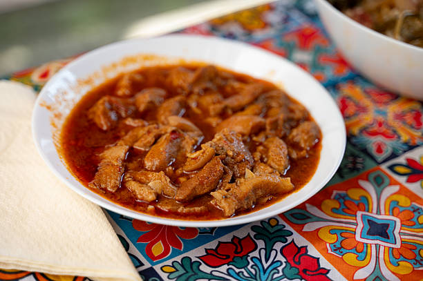 A bowl of traditional Hungarian tripe stew served in a white dish atop a colorful patterned tablecloth. The rich, paprika-spiced sauce coats tender slices of tripe, offering a rustic and hearty Eastern European culinary experience.