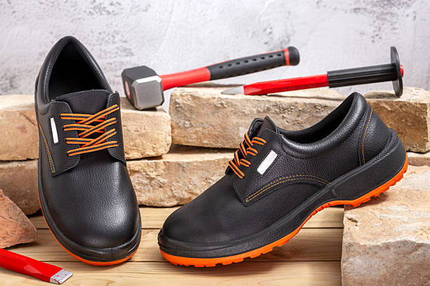 A pair of new work shoes and a sledgehammer with chisels leaning against old bricks lined up on a wooden table. Selective focus.