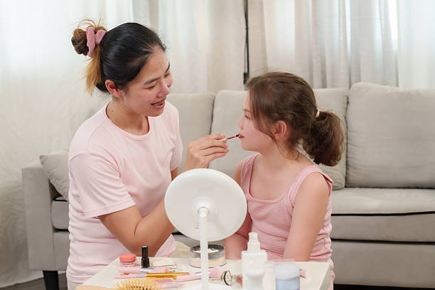 istock Asian single mother smiling while gently applying lip color to daughter during beauty session, mother and child sharing close bond, happiness and nurturing seen, parenting support and care. 2221232321