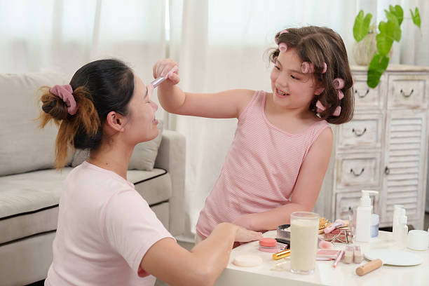 istock Asian girl laughing while playfully applying makeup on mother during cheerful beauty session, strong family connection, nurturing trust, joyful parenting and affection in cozy warm home setting 2221232349