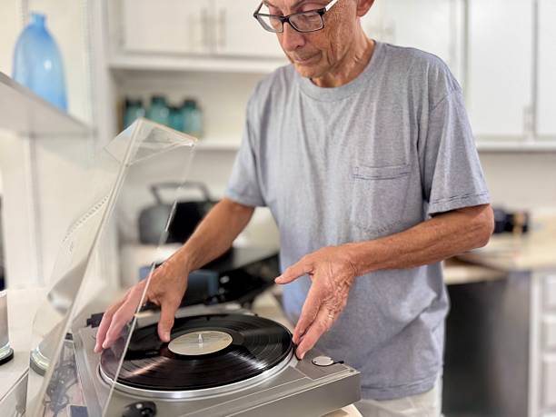 istock Senior man with eyeglasses putting record on older turntable in home 2221234091