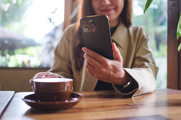 istock Closeup image of a woman holding and using mobile phone while drinking coffee in cafe 2221238767