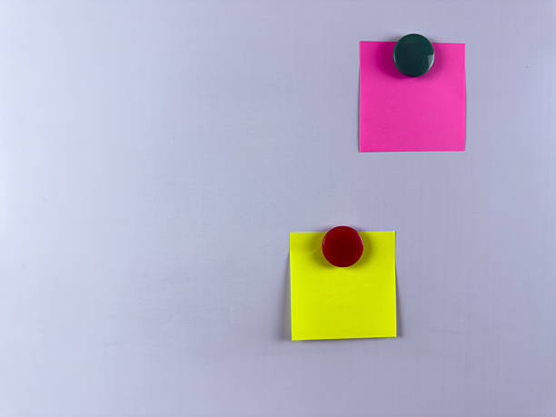 istock Pink and yellow sticky notes secured with magnets on whiteboard ideal for reminders planning and organization in office school or home environments. Enhancing efficiency and creativity 2221264582