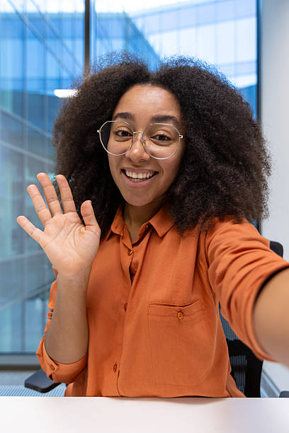 istock A woman smiles and waves during a video call on her smartphone while in a modern office space with natural light. 2221269285