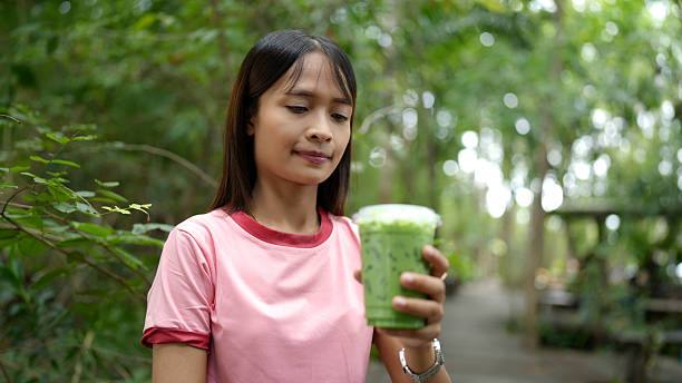Young woman in pink shirt is enjoying green beverage while surrounded by lush greenery, conveying sense of relaxation and refreshment