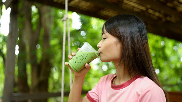 Young woman enjoys refreshing green beverage while sitting outdoors, surrounded by lush greenery. serene atmosphere enhances experience