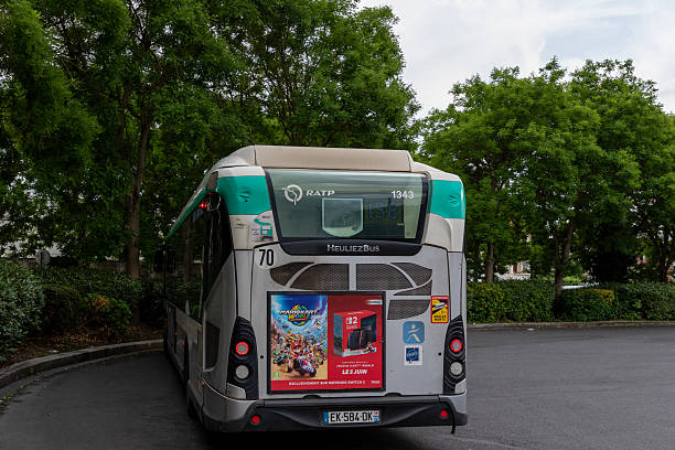 The rear of a parked RATP Heuliez Bus number 70 is shown, adorned with ads for Nintendo Switch and Mario Kart, with green trees in the background. Paris, France  - June  06, 2025.