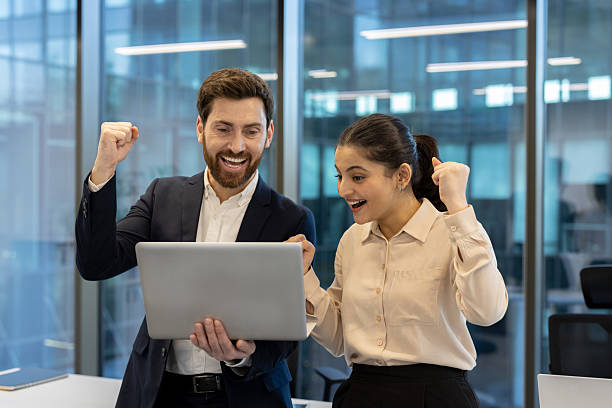 istock Excited colleagues celebrate a win together, looking at a laptop in a modern office setting. 2221280810
