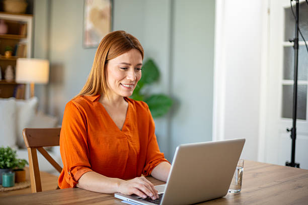 istock Smiling woman working from home on laptop at dining table 2221287723