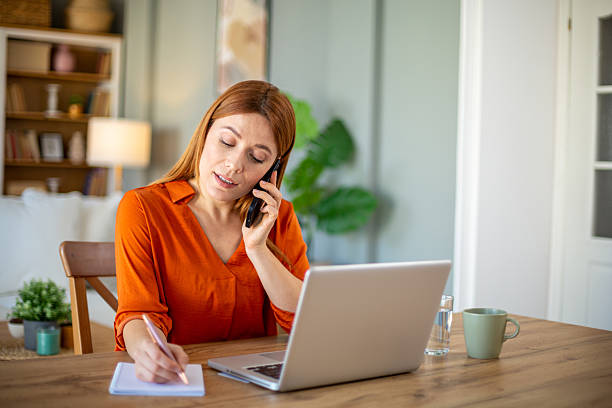 istock Focused businesswoman taking notes while talking on phone at home office 2221288212