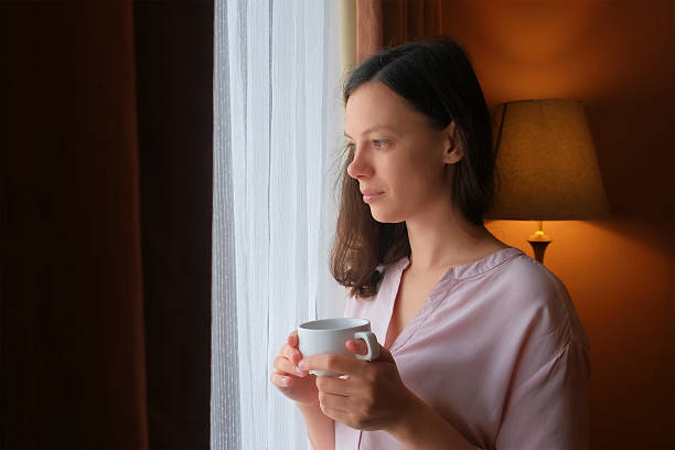 istock Brunette woman drinking tea standing looking at window smiling enjoying pastime. 2221290270