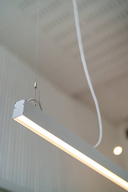 Close-up of a minimalist rectangular LED ceiling light fixture suspended by cables, with a soft glow illuminating the modern indoor space.