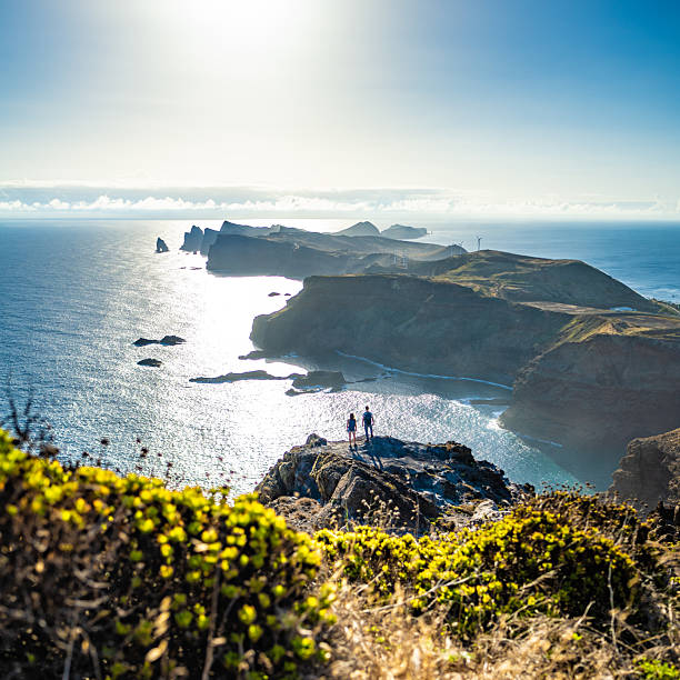 istock Backpacker couple enjoys panoramic view from steep cliff over seascape and along rugged foothills of Madeira coast at sunrise. Ponta do Bode, Madeira Island, Portugal, Europe. 2221303175