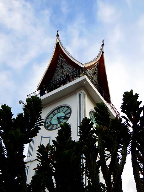 Bukittinggi, Indonesia - Dec 30, 2017: A low angle shot of Minangkabau Big Clock (Jam Gadang) and the cactus silhouettes against cloudy sky.