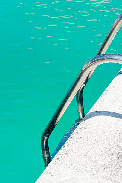 sunlight sparkles on turquoise pool water by a metal ladder