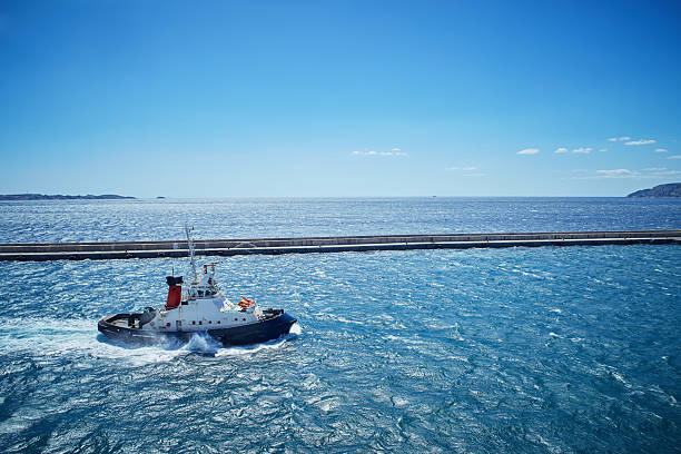 Marine tugboat heading out from harbor into rough sea, powerful waves and clear skies