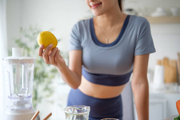 istock Woman holding a fresh lemon while preparing ingredients for a healthy vegetable smoothie in a kitchen. 2221334873