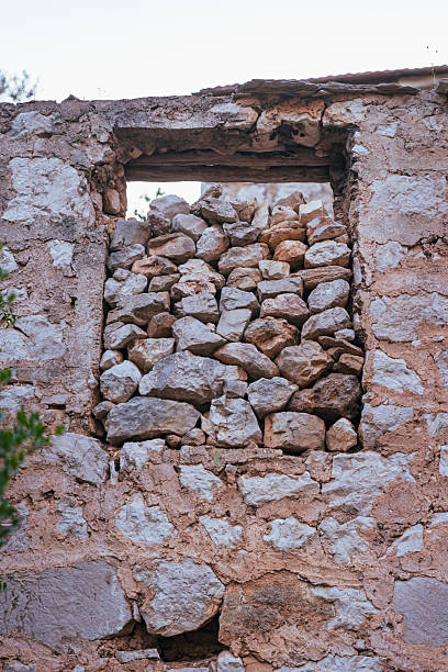 Close-up image of an old stone wall with a sealed window in the abandoned village of Malo Grablje on Hvar Island, Croatia. The rough texture of hand-laid limestone rocks and earthen mortar showcases traditional Mediterranean construction methods, typical of centuries-old Dalmatian homes. A compelling visual metaphor of time standing still, decay, and preservation.