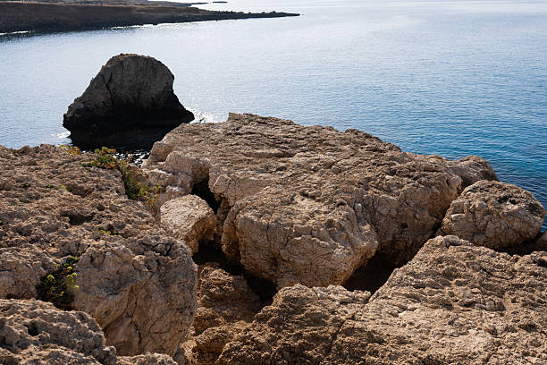 summer beach with rocks and stones. Clean clear water and blue. View on pile of stones in water of Adriatic sea partly in shadow, partly lit with sunlight near huge rock blue sky