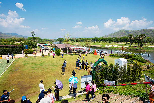 Thai people in open landscape at railway Tha Chomphu Bridge in Lamphun province built in 1919 next to the Khun Tan Tunnel. Bridge crosses the Tha River and passes through the middle of an open field and landscape  scenery. Bridge is not made with steel but  it has a reinforced concrete frame of 87.3 metres long. Train has stopped and people are going to lookout and at river Tha. View from railway tracks level into open field