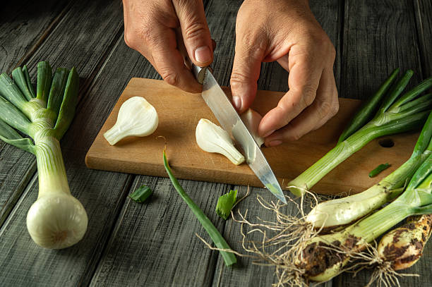 istock Hands skillfully slice fresh green onions on a cutting board. The rustic kitchen setting is enhanced by the wooden surface and natural light, highlighting the vibrant vegetables 2221349432