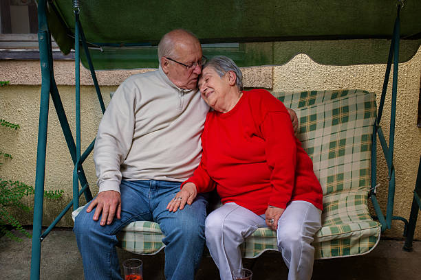 Mature married couple sitting on a bench in their backyard, they are wrapped in  blanket, enjoying the view, hugging, looking happy and relaxed.