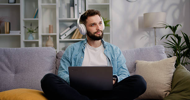 istock Businessman wireless headphones sit on sofa using laptop at home Creative young man browsing internet and managing social media. E-learn with e tutor, improve knowledge use videocall, modern tech concept. 2221360383