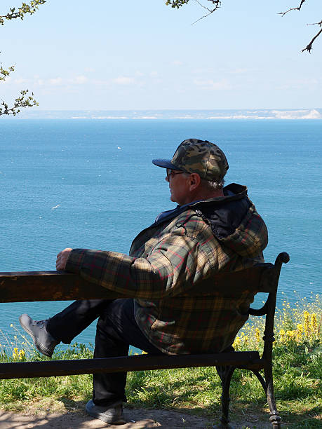 istock man sitting on a bench and looking at the sea panorama, rear view 2221365714