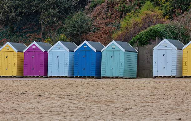 istock A row of brightly colored beach huts stand on a sandy beach against a backdrop of greenery. 2221370304
