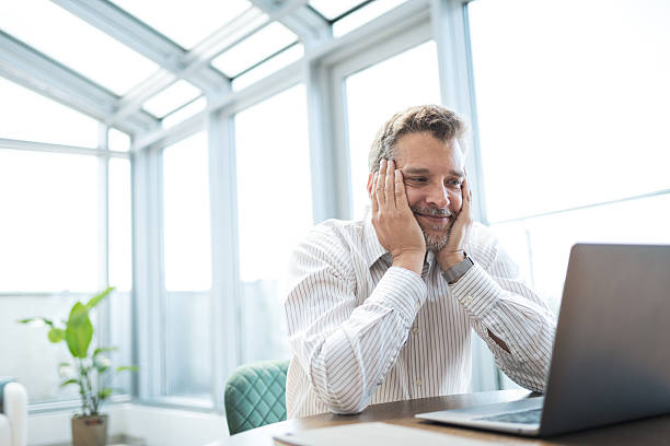 istock Man smiling while looking at laptop in a bright modern office 2221370361