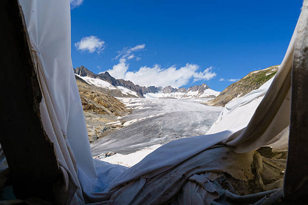 View from below, through a fabric-covered ice tunnel, onto a Rhone glacier top.  Due to rising global temperatures Rhone Glacier has lost nearly 50% of its volume . To slow down its melting during summer scientists covering part of it with the special reflective thermal blankets. Fabric helps reduce heat absorbation and limits ice loss by up to 70% in the covered areas