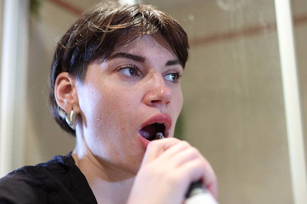 Woman using electric toothbrush for cleaning teeth, promoting oral hygiene and daily routine