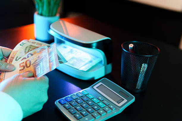 istock Cashier counting euro banknotes and verifying authenticity using detector machine 2221388442