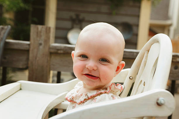 A baby girl, seven months old sitting in a wooden highchair on a back deck. Shot with a Canon 5D Mark IV.