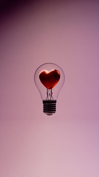 istock Light bulb with heart shaped filament inside glass bulb with metal base and support wires on pink background 2221391532