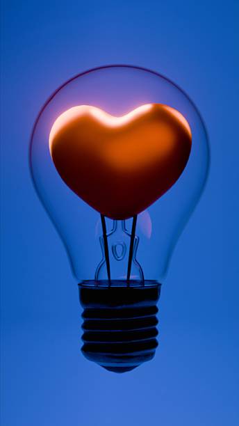istock Light bulb with heart shaped filament inside glass bulb on blue background 2221391540
