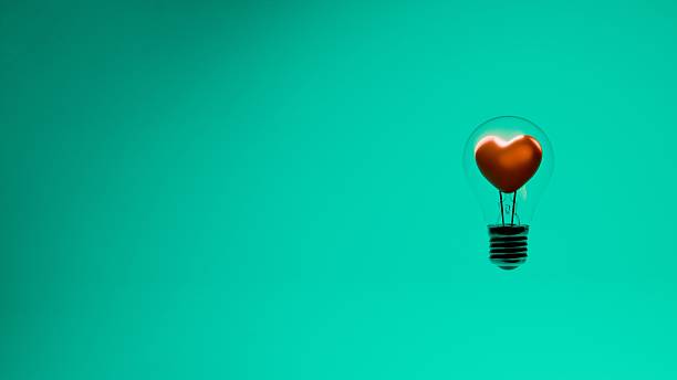 istock Light bulb with heart shaped filament inside glass bulb on green background 2221391543