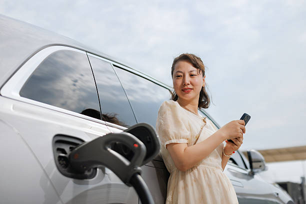 istock Woman using mobile phone while charging electric car 2221401184