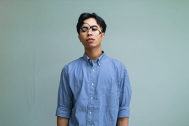 Stressed young Asian man making a funny, messed-up face while reacting to pressure, isolated on a plain background with humorous and expressive mood