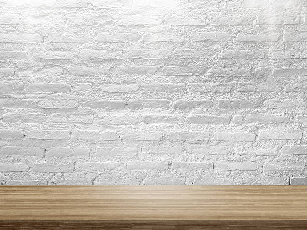 istock empty wooden table top in foreground with rustic white brick wall and light from above at background. 2221428682