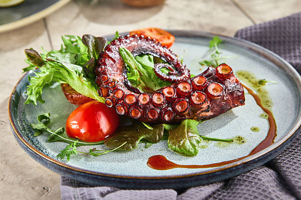 istock Grilled octopus tentacle with mixed greens under bright natural light, rustic overhead composition 2221430928
