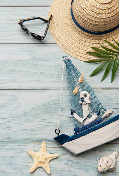 istock Seashells, sunglasses, straw hat, starfish and decorative sailboat creating summer holiday atmosphere on wooden planks 2221436057