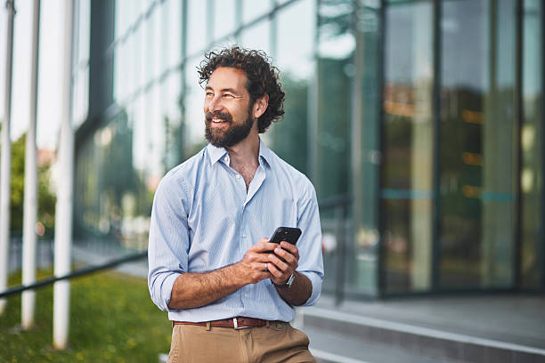 istock Smiling businessman using smartphone outside office building 2221439442