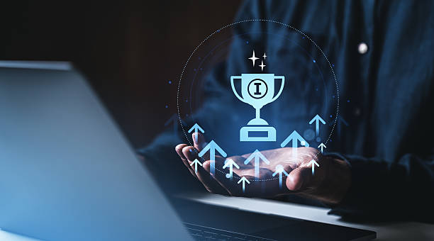 istock Digital trophy icon hovering above open hands with growth arrows and laptop on dark background, symbolizing success and achievement in business technology. 2221443858