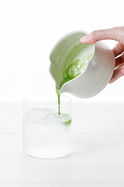 fresh matcha tea, green tea pouring on a glass of coconut water on white wooden table.
