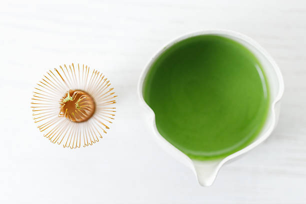 Cup of fresh matcha tea, green tea and Chasen, bamboo whisk, on white wooden table.