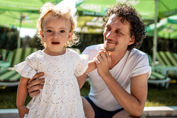 istock Smiling Father Holding Daughter Outdoors in a Sunny Green Environment 2221448417