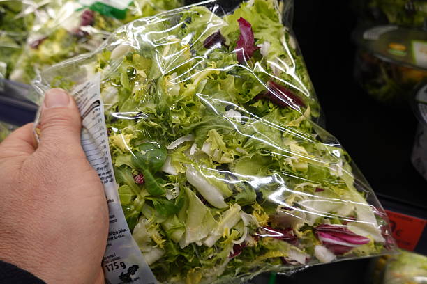 Hand holding a bag of fresh mixed salad in a supermarket, reading the nutritional information label